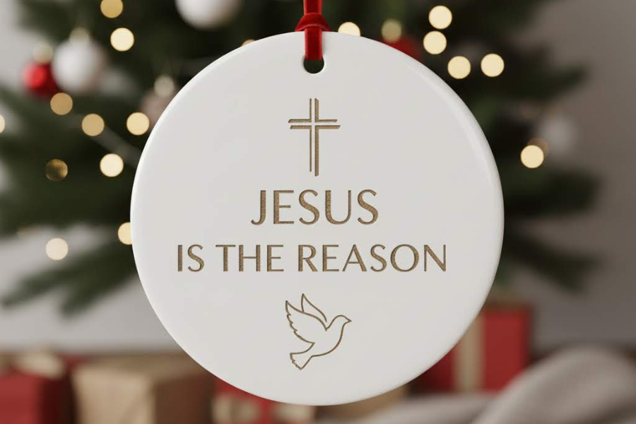 Decorative Christmas ornament with 'Jesus is the Reason' text and cross, dove, and star of David symbols on a blurred Christmas tree background.