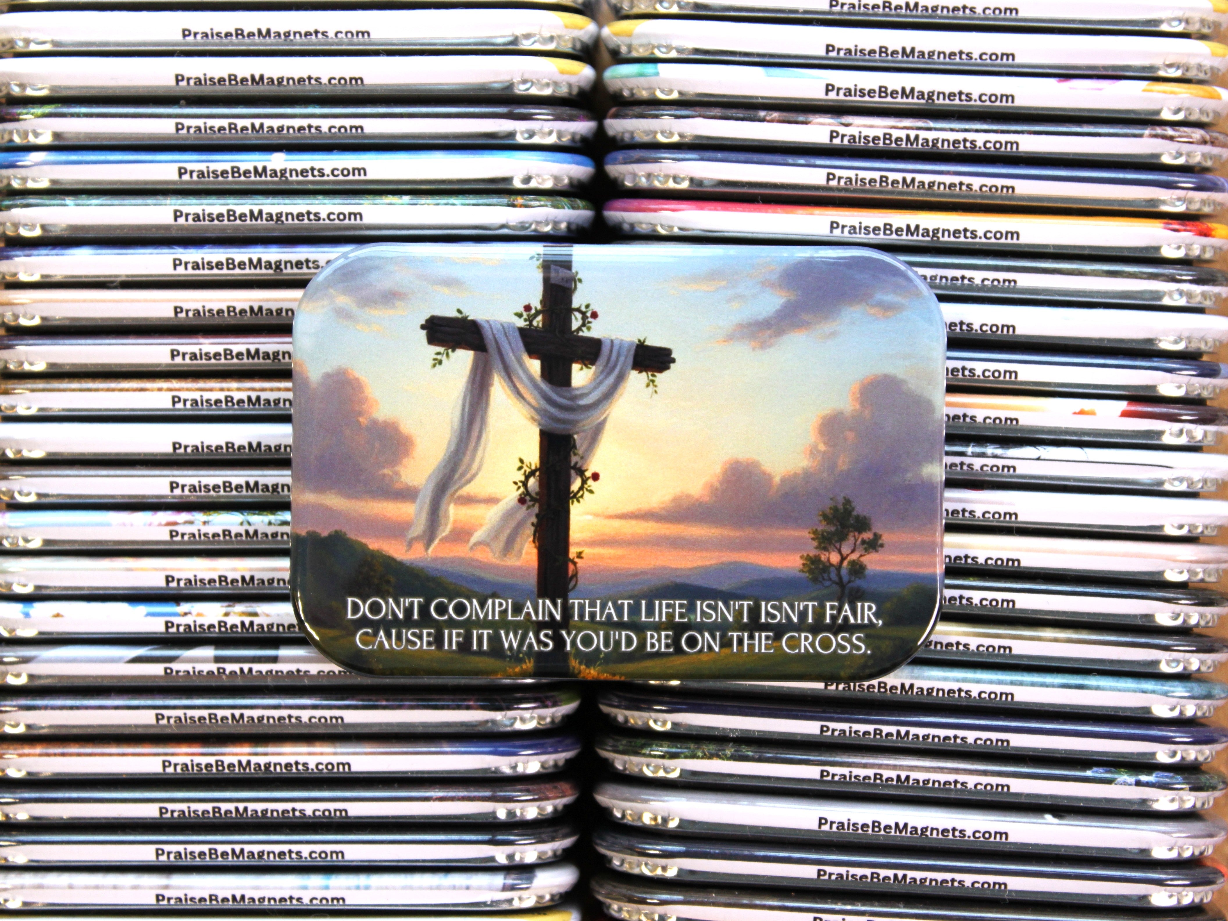Stack of 'Praise Be Magnets' with a magnet featuring a cross and sunset design.