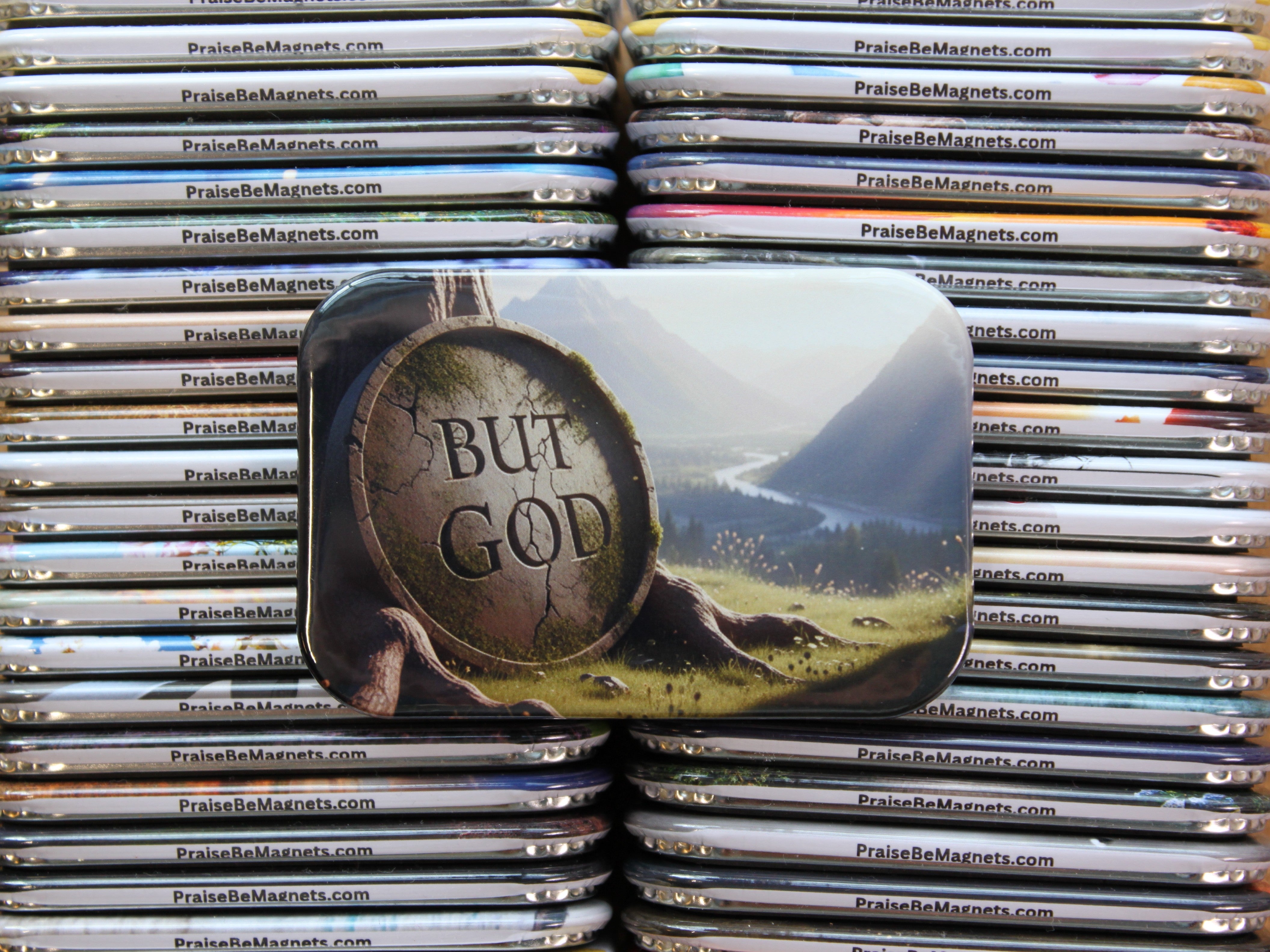 Stack of metal magnets with a prominent magnet featuring 'But God' and a landscape design.