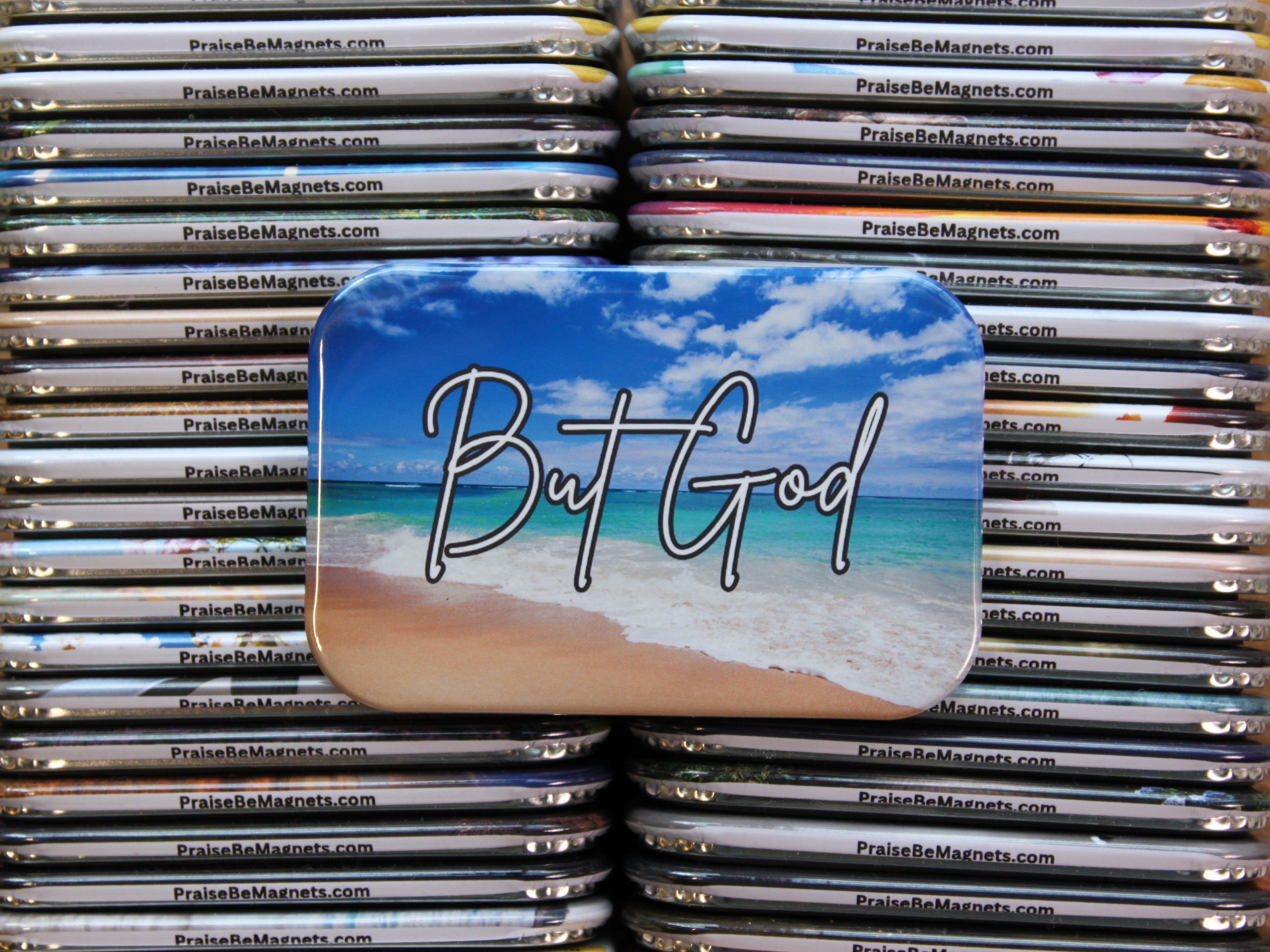 Stack of 'PraiseBeMagnets' products with a prominent magnet featuring 'But God' text on a beach background.