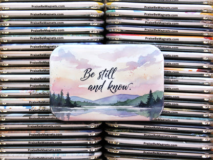 Stack of 'Praise Be Magnets' with a scenic magnet featuring 'Be still and know.' text.