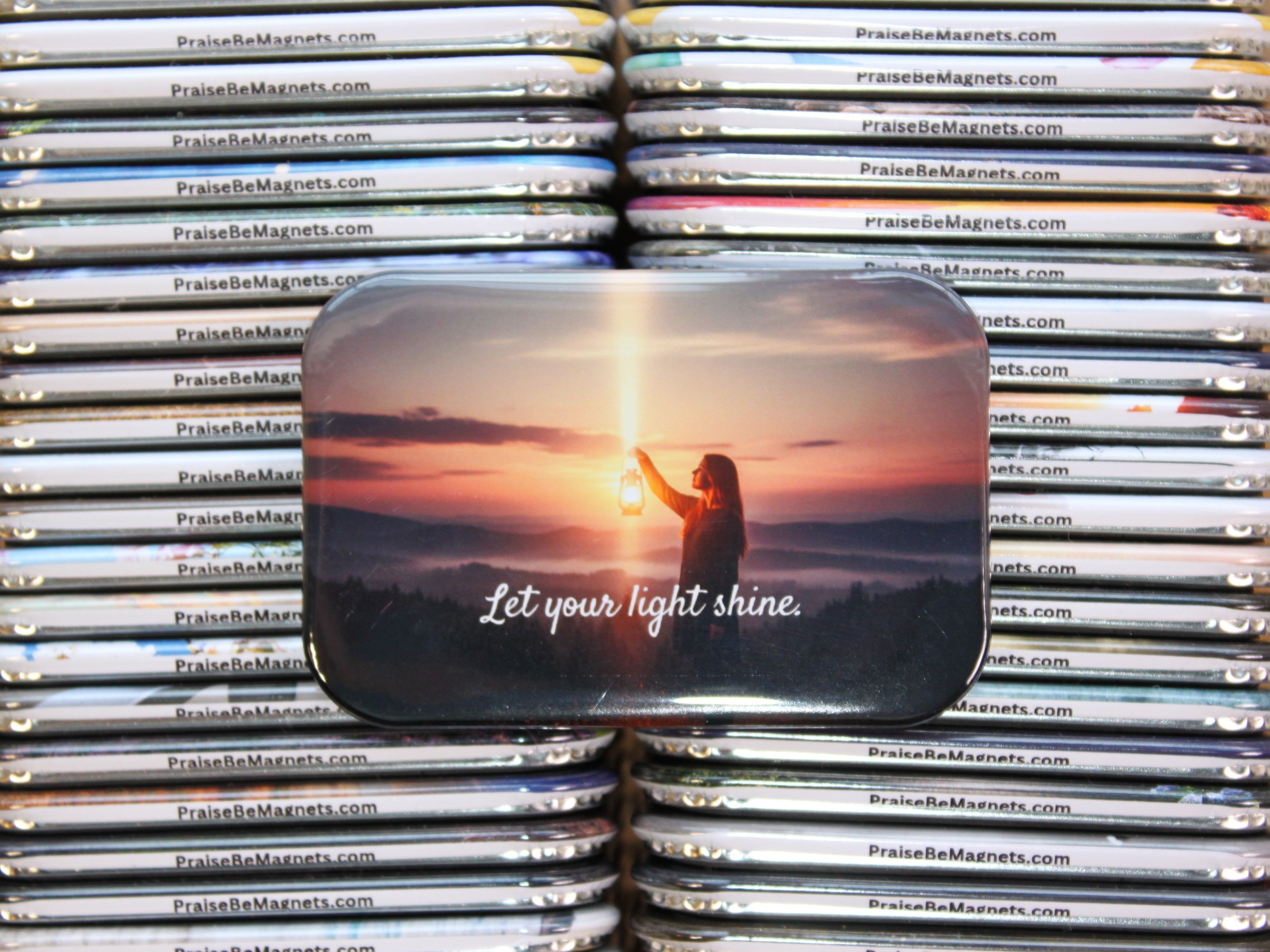 Stack of metal magnets with a design of a person holding the sun and the text 'Let your light shine' on a magnetic strip.