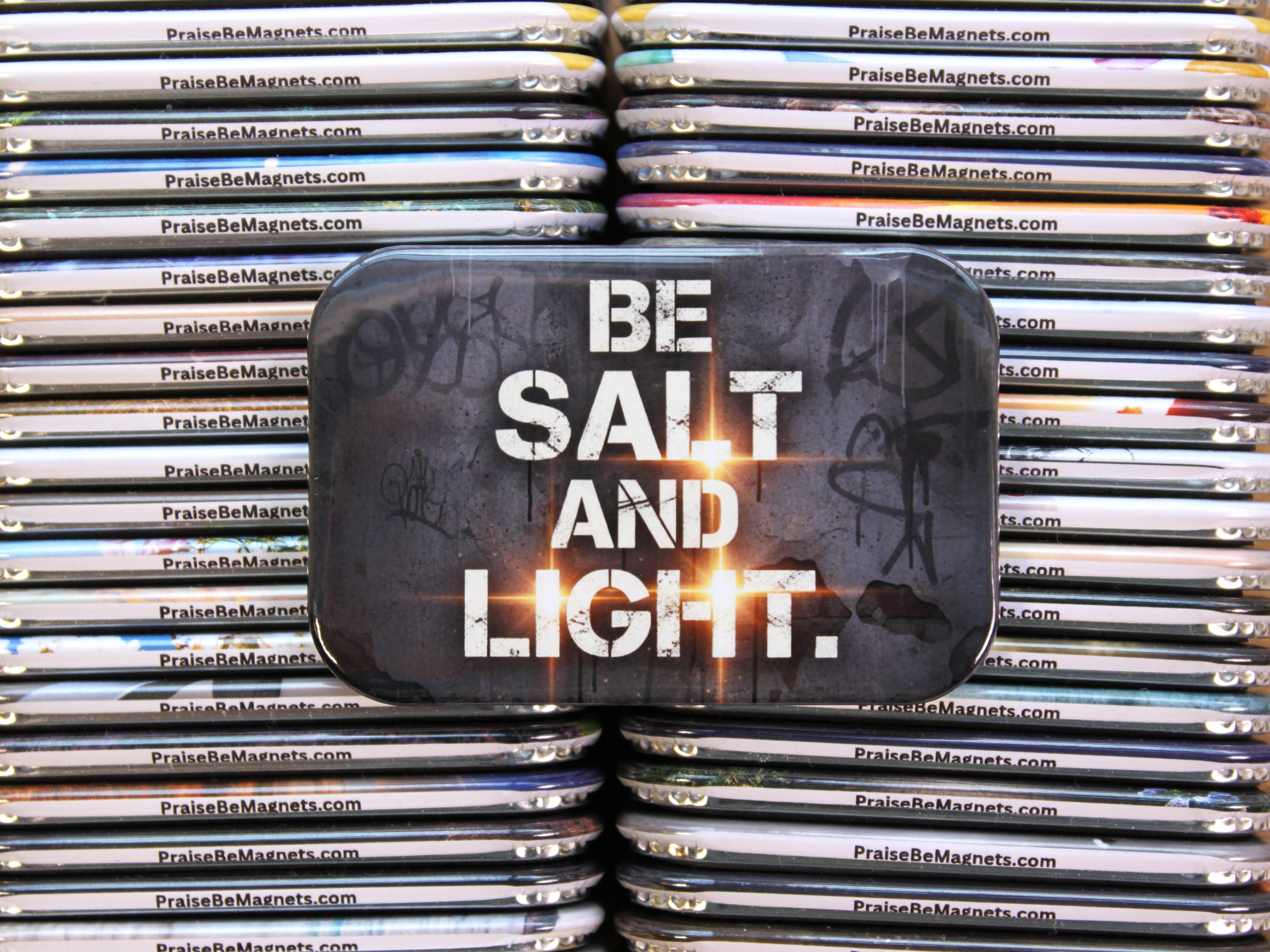 Stack of metal magnets with 'Be Salt and Light' text on a reflective surface.