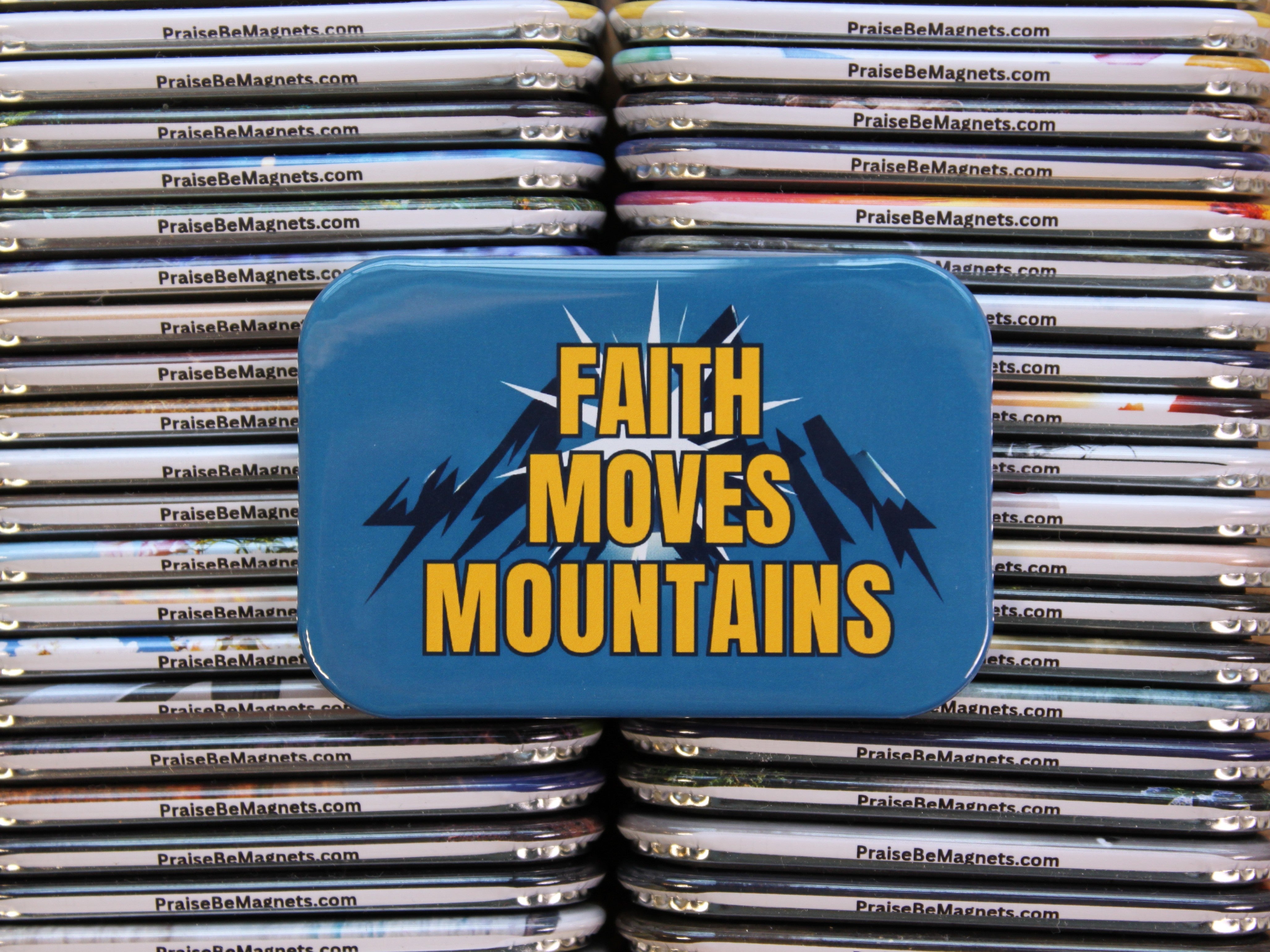 Blue tin with 'Faith Moves Mountains' text on a stack of metal magnets.