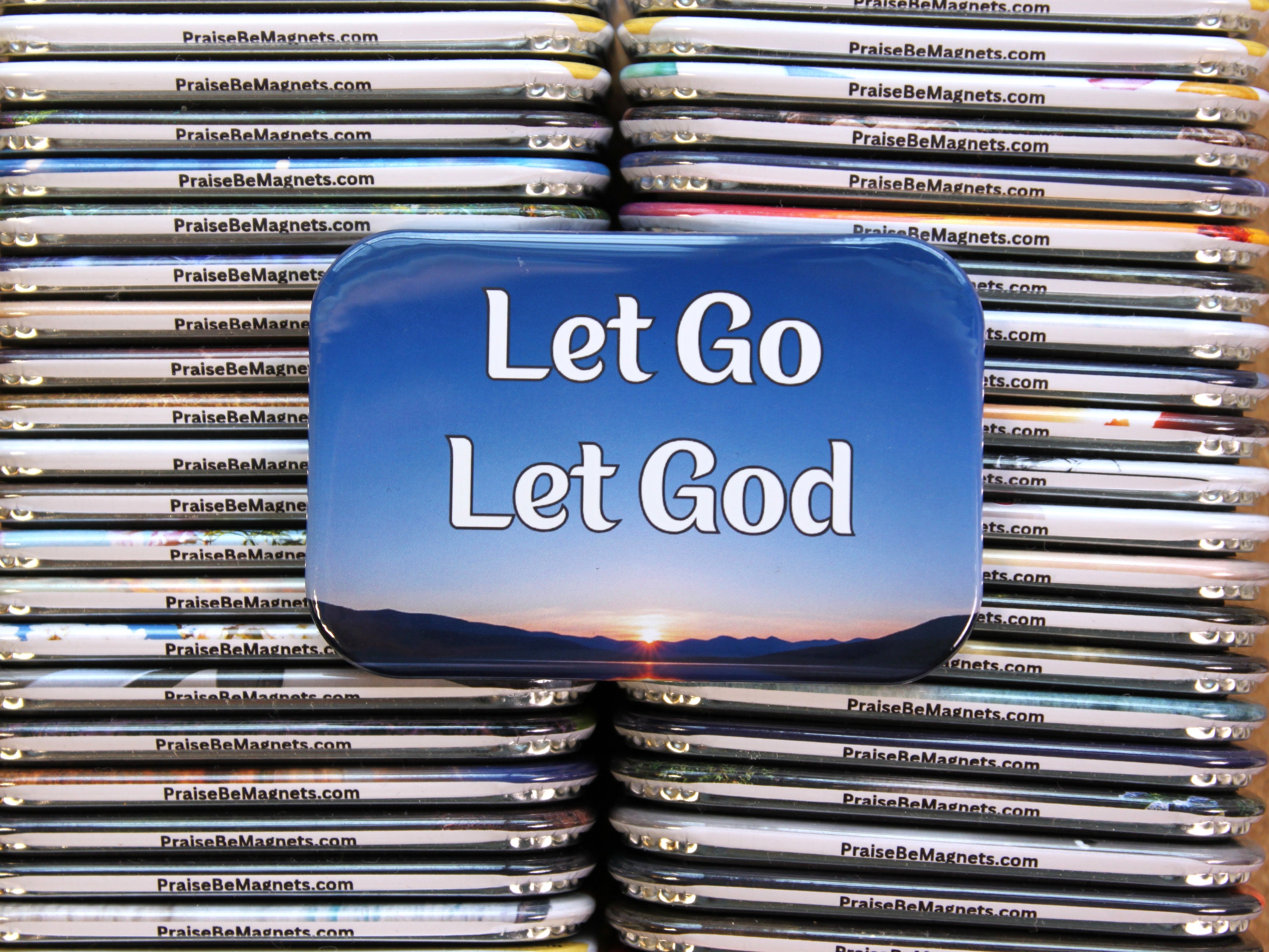 Stack of 'Let Go Let God' magnets with a scenic design on top