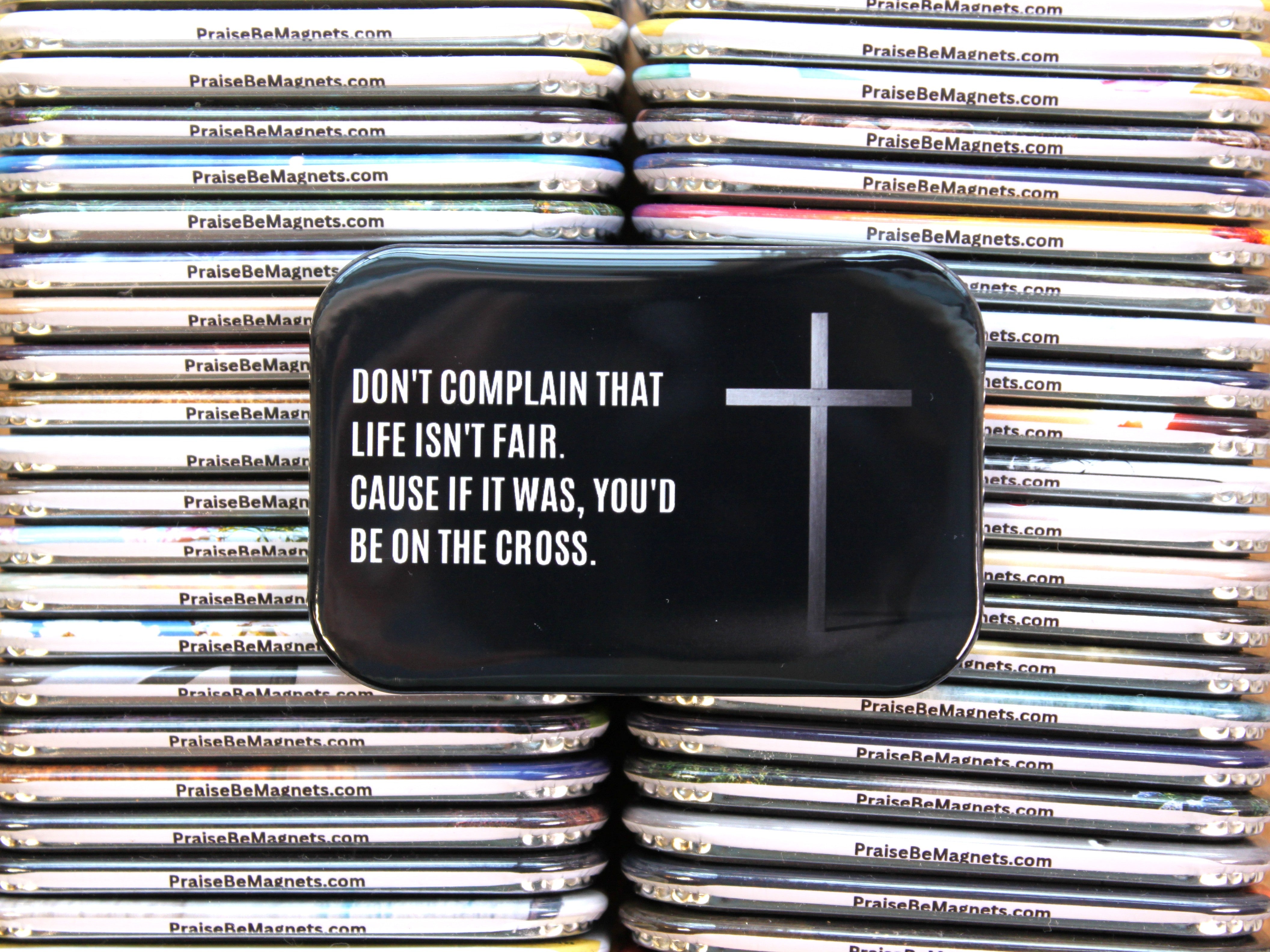 Stack of black containers with motivational text and a cross symbol, branded 'PraiseBeMagnets.com'.