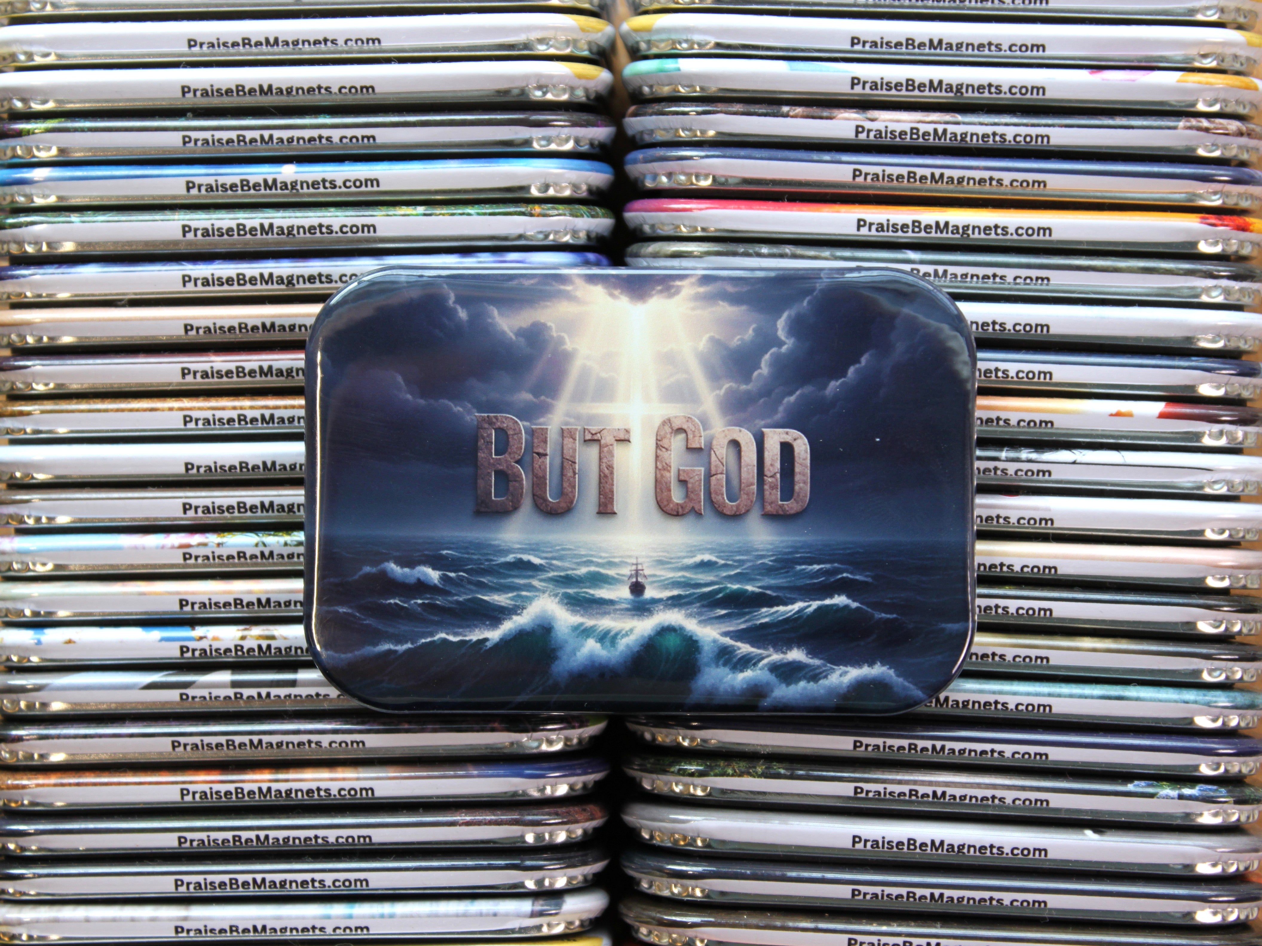 Stack of 'PraiseBeMagnets' with a prominent magnet featuring 'But God' text and a ship in the ocean.